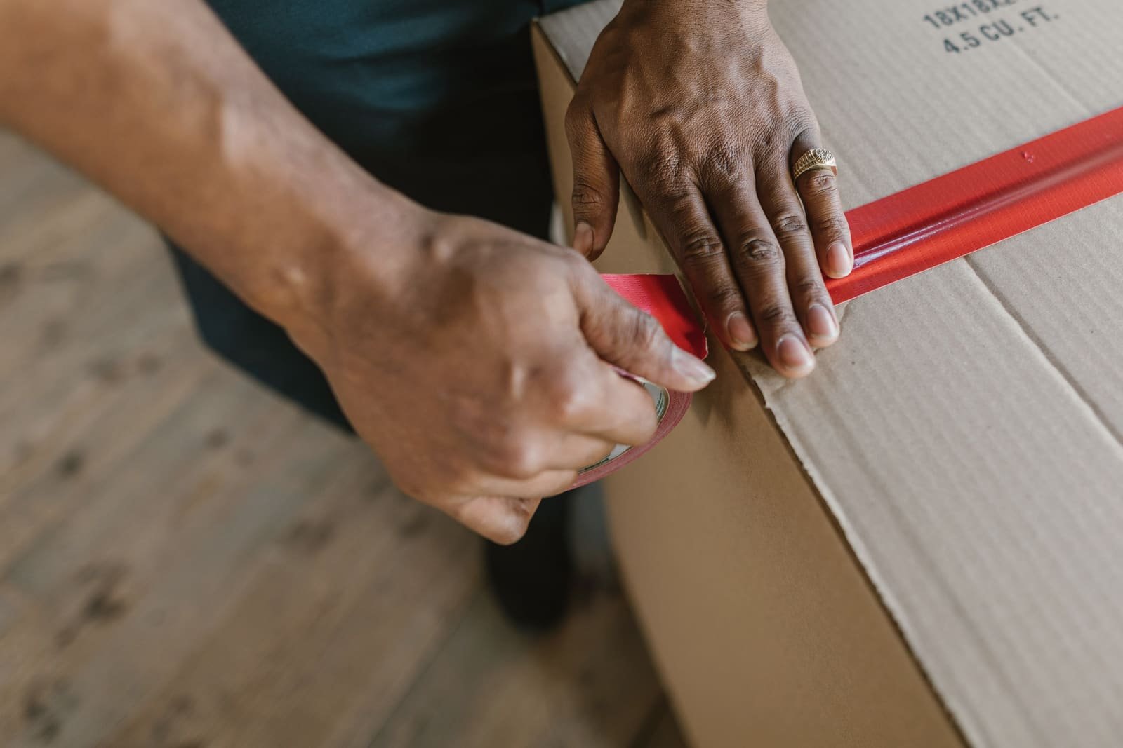 Hands sealing a cardboard shipping carton with a strip of red packing tape