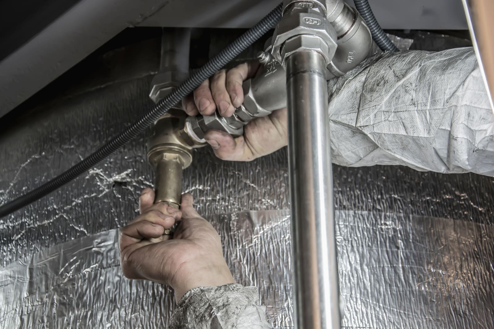 Hands tightening brass and steel pipe fittings in a tight space under a fixture