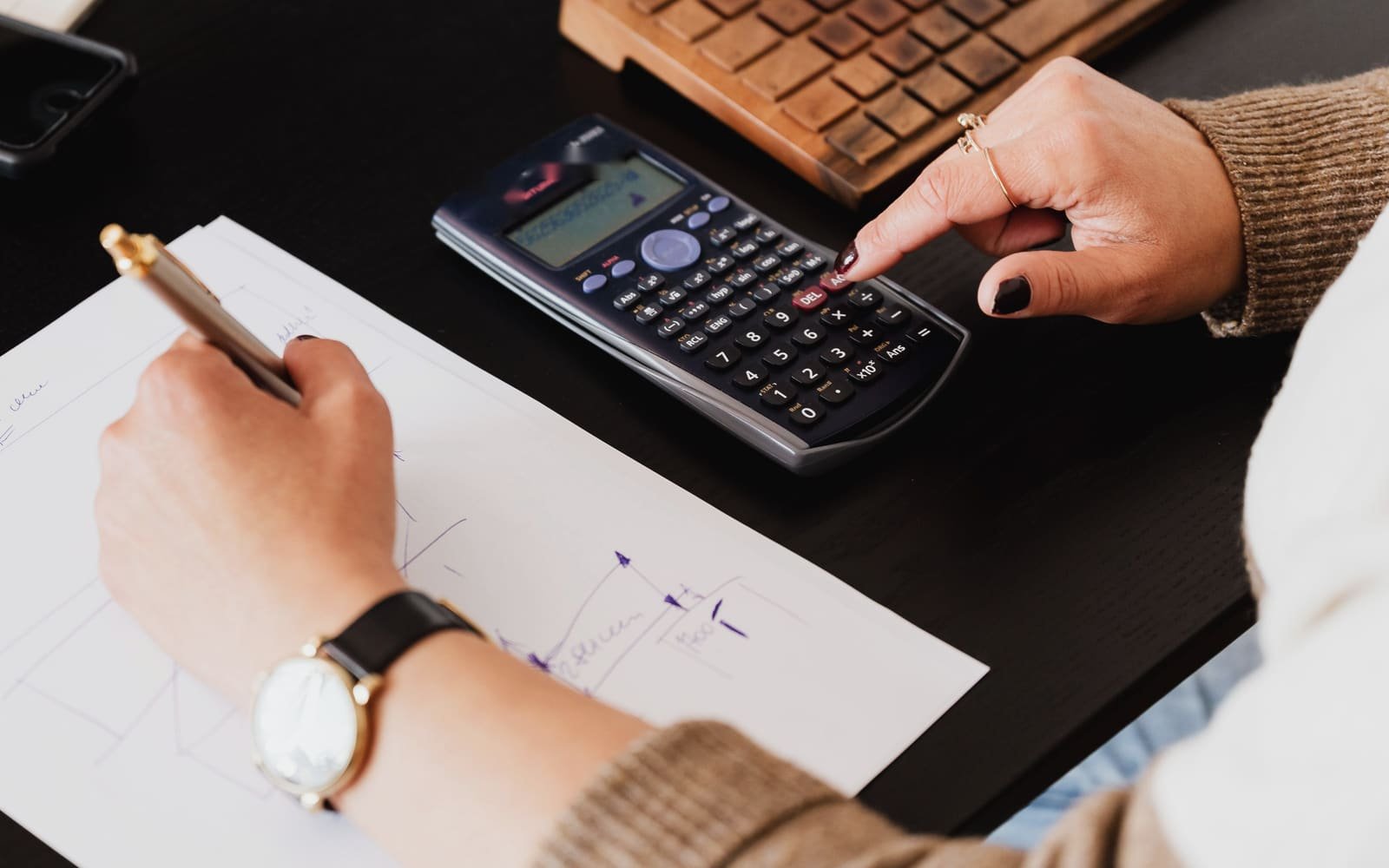 A hand keying figures into a calculator beside a sheet of handwritten notes