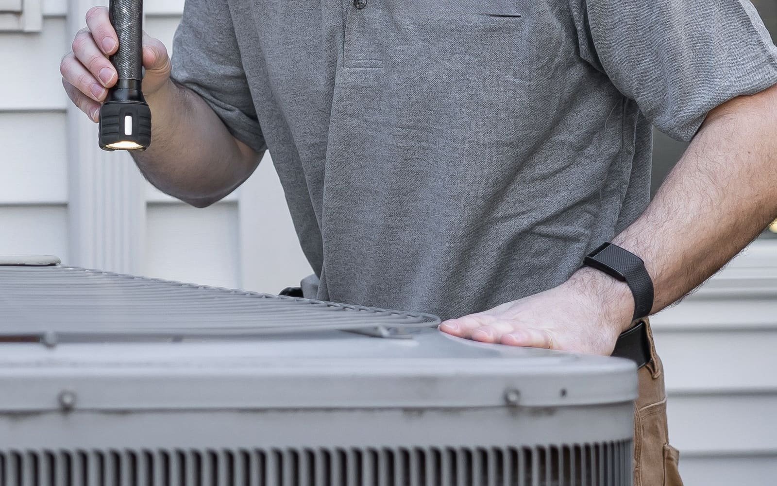 A hand resting on top of an outdoor air-conditioning condenser during a service check