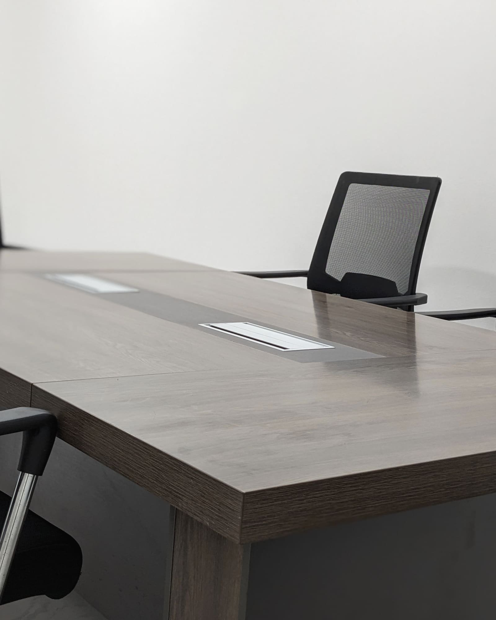 An empty conference table with mesh chairs against a plain white wall