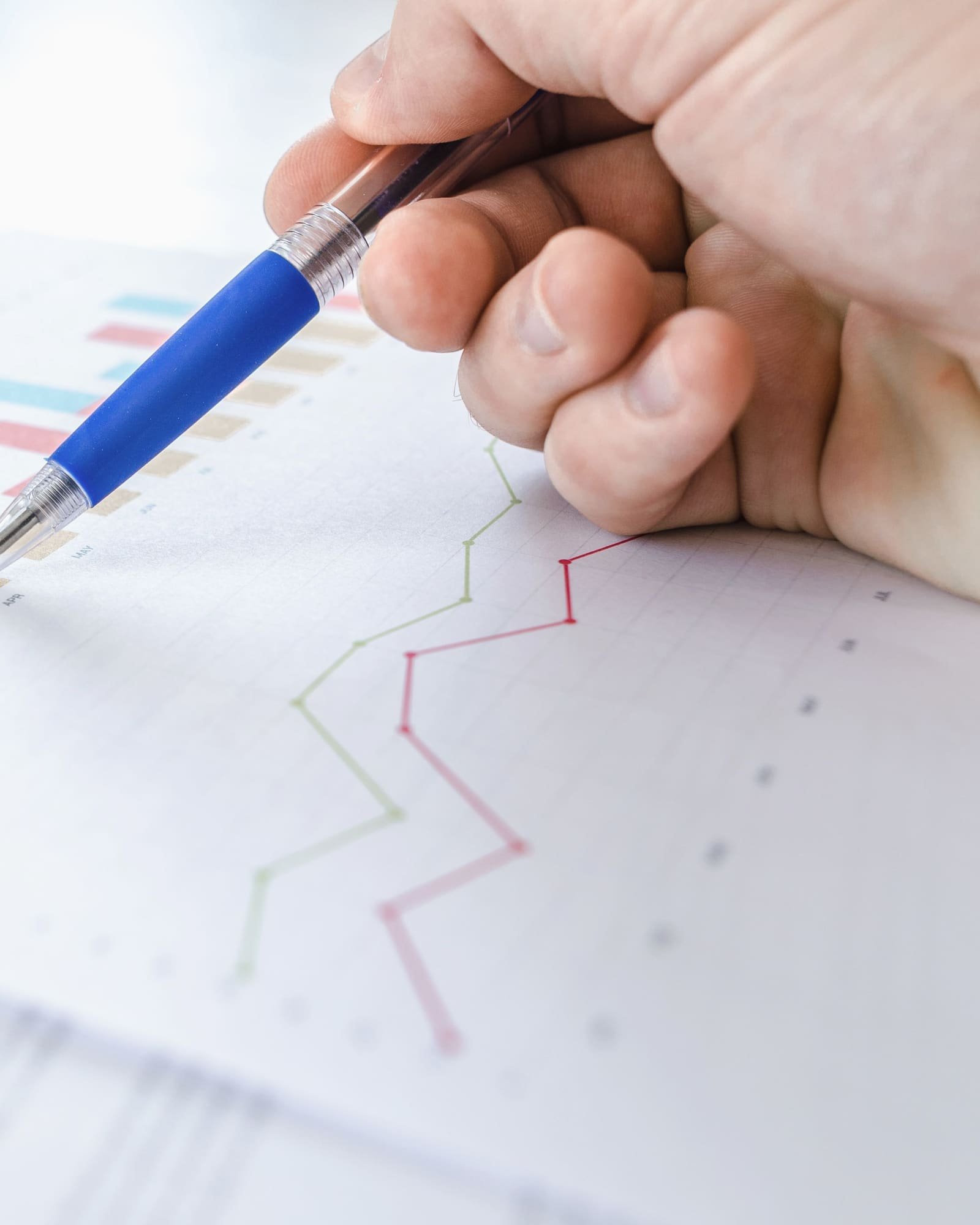 A hand with a pen pointing at printed line and bar charts